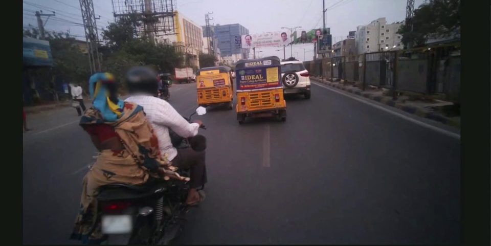 A two-wheeler rider's view of Hyderabad traffic: a scooter rider ahead, an auto-rickshaw, and oncoming vehicles
